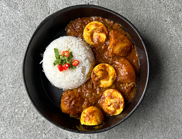 delicious plate of rice with spicy chicken and egg curry served in a bowl featuring garnishes of herbs and red chili for an appealing food presentation